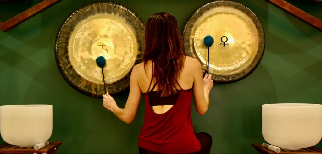 Jamie Bechtold playing two gongs seated at The Soundbath Center
