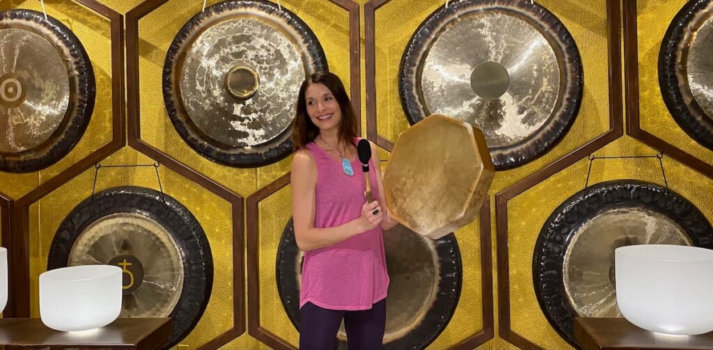 Jamie Bechtold playing shamanic drum in front of gongs at The Soundbath Center